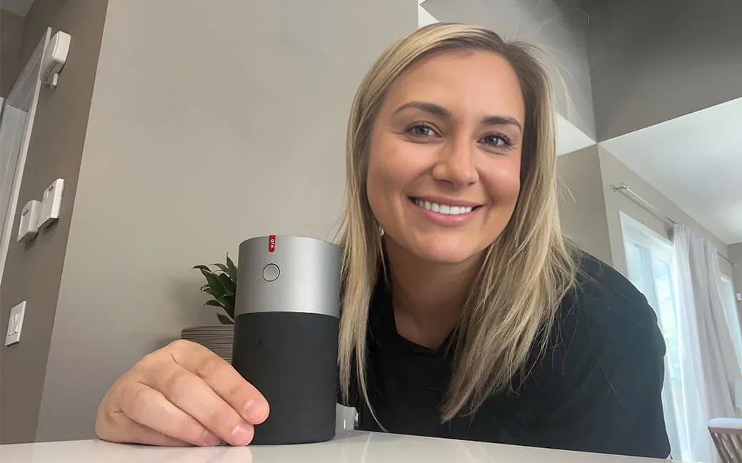 Una donna sorridente a un tavolo, con la mano sull’umidificatore EvenBreeze da cui sale la nebbiolina