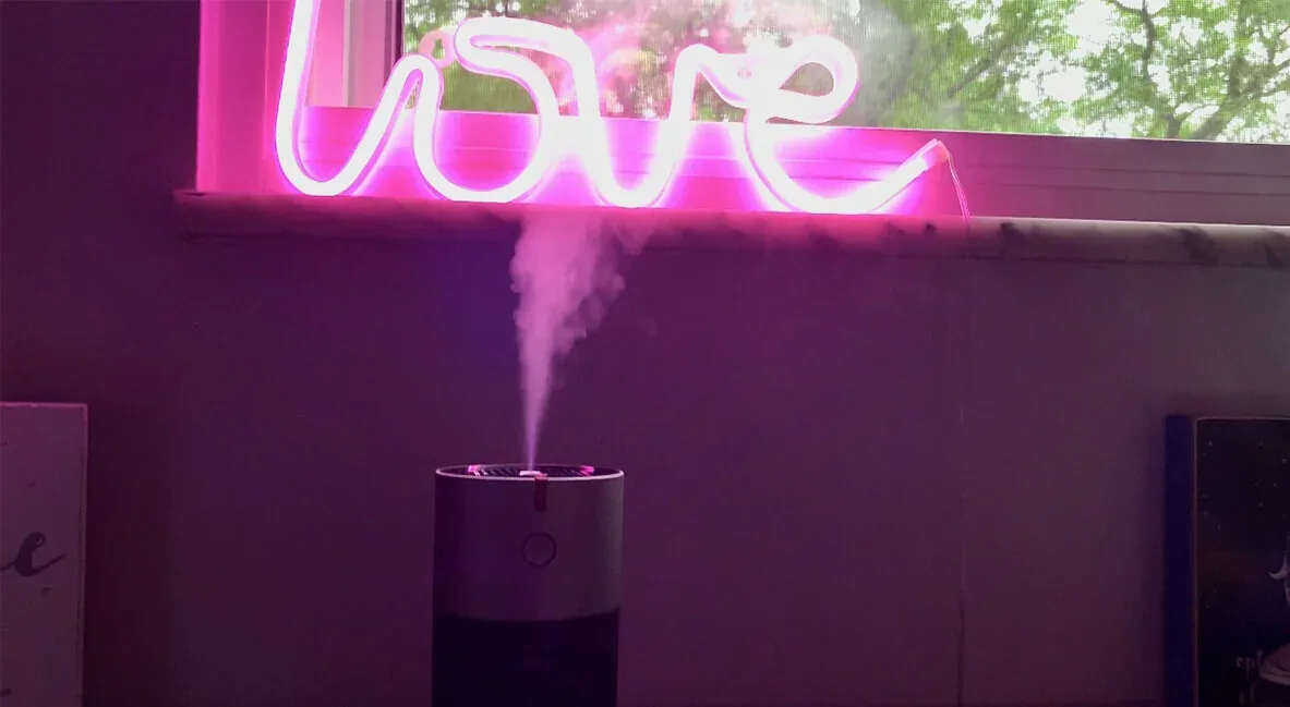 L’umidificatore EvenBreeze acceso su un tavolo, sotto un’insegna al neon rosa con la scritta love